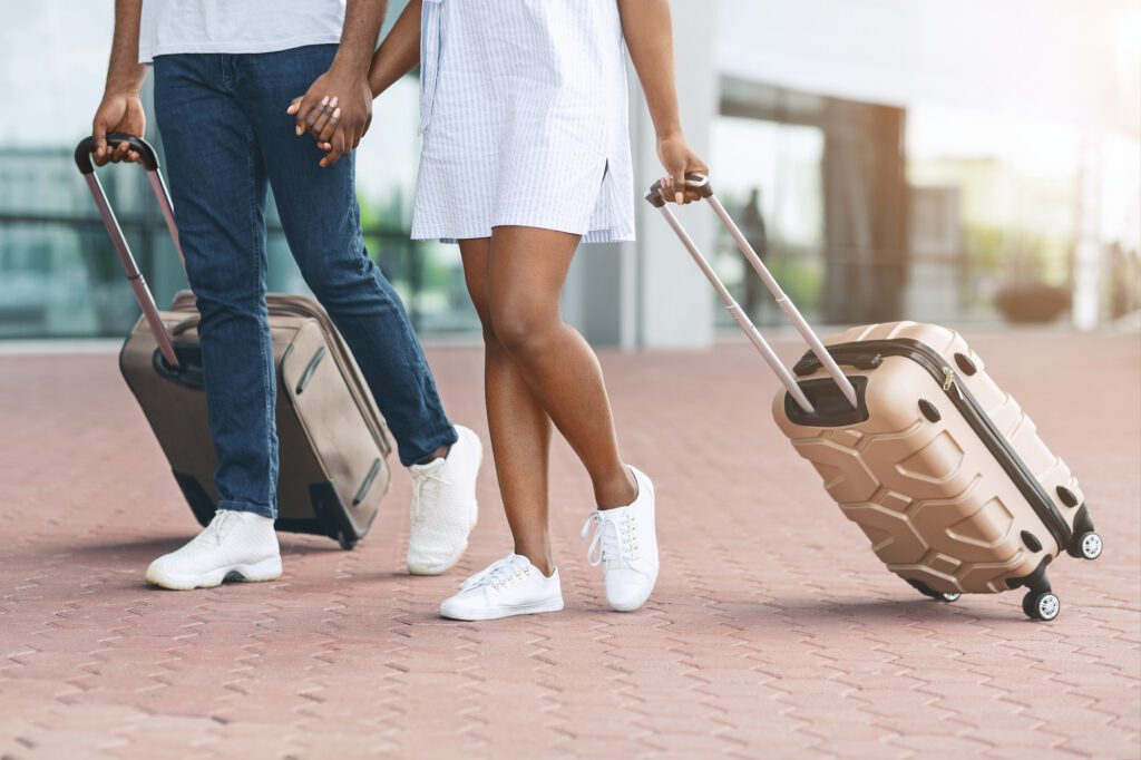 Unrecognizable afro couple walking with luggage outside of airport